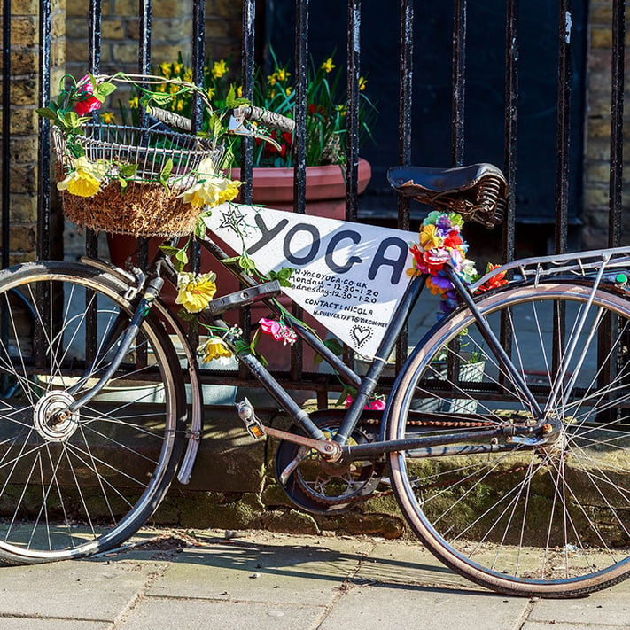 Bike with yoga sign and flowers leant against a fence