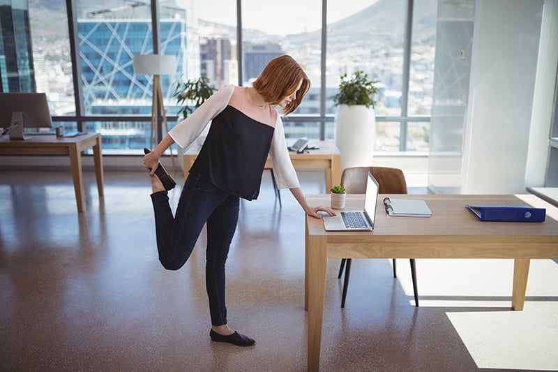 woman leaning over computer while stretching